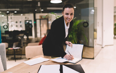 Cheerful businesswoman making notes in diary at office