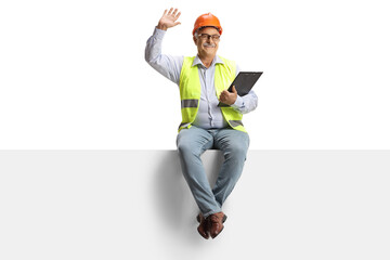 Wall Mural - Full length portrait of a mature male engineer sitting on a blank panel and waving at camera