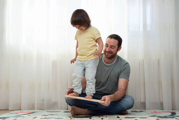 Little girl balancing on a balance board with her father's help.