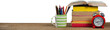 Stack of books by mug with colored pencils and alarm clock on wooden table