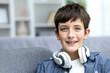 Close-up portrait of young schoolboy boy at home, teenager smiling and looking at camera in living room, wearing headphones.