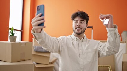 Wall Mural - Young hispanic man having video call holding keys at new home