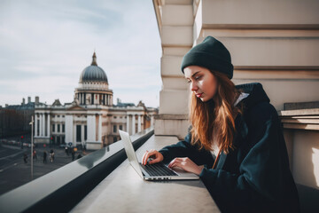 Wall Mural - Young woman sitting in London and doing work on laptop. Student or freelancer lifestyle. St. Paul's Cathedral in the background. High quality generative ai