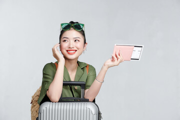 Enthusiastic asian girl shows passport tickets, smiling pleased, standing with suitcase, gray background