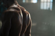 Fit muscular sweaty man with strong back muscles posing on camera at dark gym