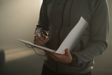 Close-up of trainer hands writing on paper with clipboard in gym