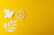High angle view of white peace sign, white dove and leaf with copy space on yellow background