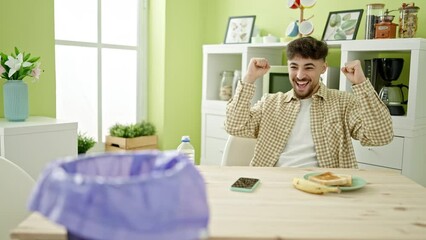 Poster - Young arab man having breakfast throwing banana peel to paper bin at home