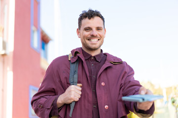 Wall Mural - Young caucasian man at outdoors holding a passport with happy expression