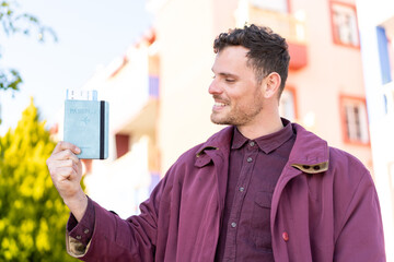 Wall Mural - Young caucasian man holding a passport at outdoors with happy expression