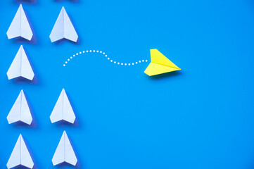 Wall Mural - Yellow paper airplane origami leaving other white airplanes on blue background with customizable space for text or ideas. Leadership skills concept and copy space