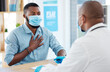 © Nina/peopleimages.com - Doctor, chest pain and patient with covid in hospital for symptoms, examination and consultation. Healthcare, sick black man and medical professional with face mask for treatment or checkup in clinic