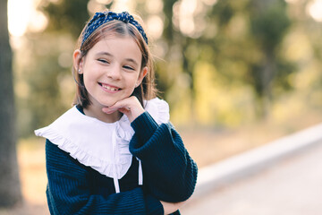 Wall Mural - Smiling funny kid girl 6-7 year old wear school uniform dress with white collar outdoor over nature background closeup. Childhood. Back to school.