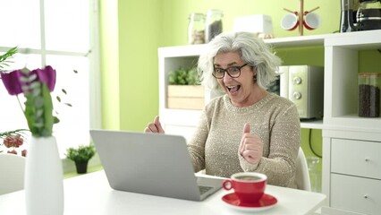 Poster - Middle age woman with grey hair using laptop sitting on table dancing at home