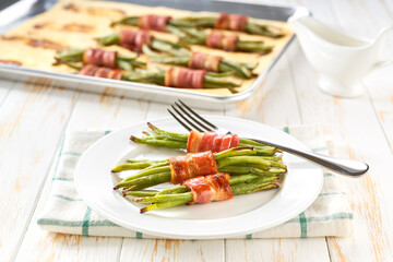 Traditional appetizer, baked  bundles of green beans wrapped in bacon in a ceramic plate on a white wooden table, close up.