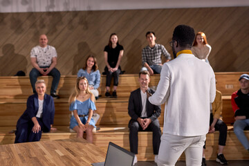 Rear view african male speaker giving talk in conference hall at business meeting event. Group of people in audience at conference hall, listening to lesson. Business and entrepreneurship. copy space