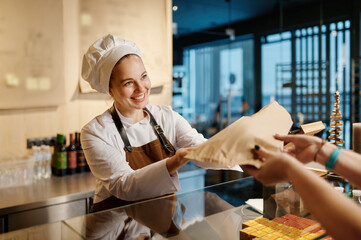 Bakery worker selling fresh tasty pastry and bread in bakery shop