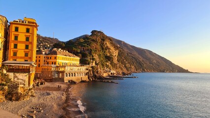 Wall Mural - Camogli, Italy - January 27, 2023: Beautiful old mediterranean town at the sunset time with illumination during winter days. People enjoying the evening at the beach with beautiful sunset background