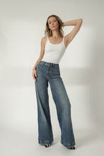 Fashion portrait of young woman in white tank top and wide leg blue jeans on the white background