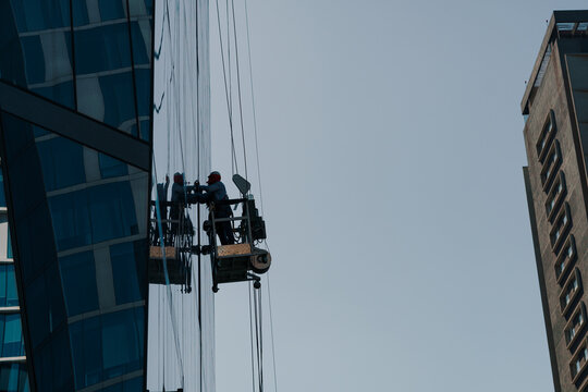 trabajador en alturas limpiando vidrios en un edificio en el centro en una grúa mecánica con cuerdas