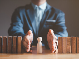 Risk management and assessment concept. Businessman prevent or protect his business and employee from high risk. Wood block represent of risk attack to business, two hands block and protect the domino