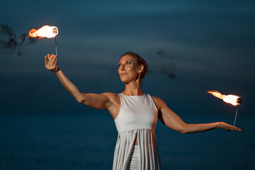 Wall Mural - Caucasian woman in a white dress juggles with fireballs in the sea. Fire and water at night. Fire show on the waterfront. High quality FullHD footage. slow motion video