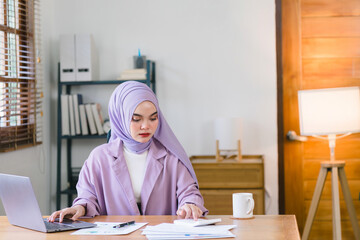 Wall Mural - stunning Asian Muslim millennial businesswoman donning a purple hijab is seen working from her home office.