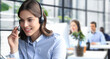 © ty - Female customer support operator with headset and smiling, with collegues at background.