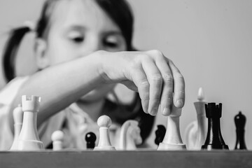 Investing in the future: training and education of the future chess champion. Beautiful child girl learns to play chess. Black and white horizontal image.