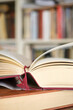 © Harry Wedzinga - Open book or textbook on a pile of closed books in front of a bookcase in a library. Education learning concept. Image with selective focus.