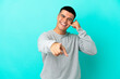 © luismolinero - Young handsome man over isolated blue background making phone gesture and pointing front