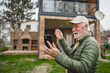 © Miljan Živković - One senior man stand in front of tiny house in day use smart phone