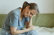 © evafesenuk - Melancholic senior woman sitting on sofa, suffering from depression, hand near head.