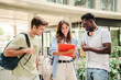 © Jose Calsina - Happy multiethnic group of teenage students talking about the homeworks after the class at university campus. Three young people smiling, having a friendly conversation together standing at the school
