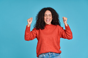 Young happy latin woman winner screaming celebrating crazy money win isolated on blue background. Excited female model feeling euphoric lucky about win or achievement with yes gesture.