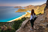 Fototapeta Góry - Hiking on Lycian way trail. Young girl with backpack enjoy view of Oludeniz beach and Blue Lagoon from Lycian way trail. Mediterranean coast. Fethiye. Turkey.