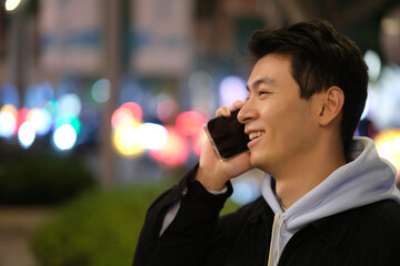 side of Chinese young man smile and on phone call at night urban city with colorful bokeh