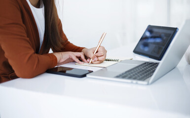 Wall Mural - Asian teenage woman sitting in white room study online class in laptop computer and tablet, video call with teacher and friends learning, university student studying online concept