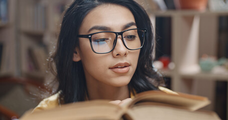 Wall Mural - Female asian student is spending her time in library, examining a book and carefully reading the contents - student lifestyle, education concept. close up