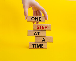 Wall Mural - One step at a time symbol. Concept words One step at a time on wooden blocks. Beautiful yellow background. Businessman hand. Business and One step at a time concept. Copy space.