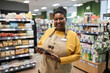 © Seventyfour - Waist up portrait of smiling black woman working in supermarket and looking at camera cheerfully