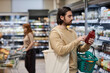 © Seventyfour - Side view portrait of bearded young man shopping in supermarket and reading ingredients label, copy space