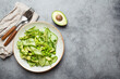 Healthy vegan green avocado salad bowl with sliced cucumbers, edamame beans, olive oil and herbs on ceramic plate top view on grey stone rustic table background. Space for text
