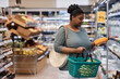 © Seventyfour - Waist up portrait of real black woman shopping for groceries in supermarket and buying dairy products, copy space