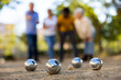 View of petanque shiny silver metal balls laying on the ground outside in the park with group of people standing behind 