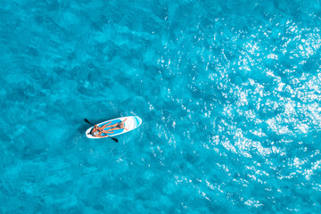 Wall Mural - Aerial view of sup board with people in blue sea at sunny summer day. Floating canoe in transparent azure water. Sardinia island, Italy. Tropical landscape. Kayak. Active travel. Top drone view. Sport