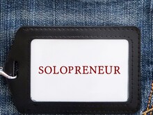 Black ID card holder on jeans background with text written SOLOPRENEUR, person who sets up and runs business on their own, works independently and doesn't hire employees