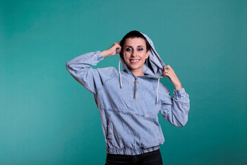 Smiling beautiful woman playing with hood while posing funny in studio over isolated background. Confident gorgeous with trendy makeup looking at camera making positive expression