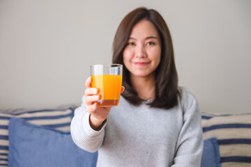 Wall Mural - Portrait image of a young woman holding and drinking fresh orange juice at home