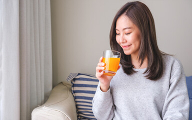 Wall Mural - Portrait image of a young woman holding and drinking fresh orange juice at home